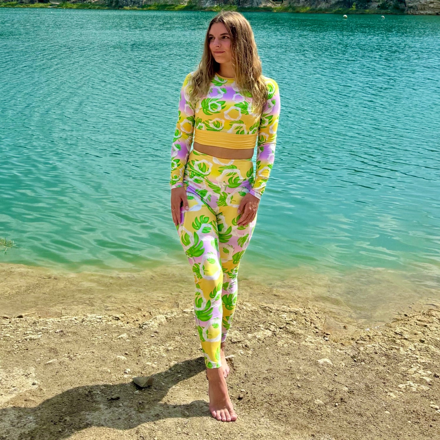 A warm golden yellow and pinky lilac sunset ombré background with megalodon jaws and monstera leaves on our Meg Monstera Recycled Cropped long sleeve rashguard
