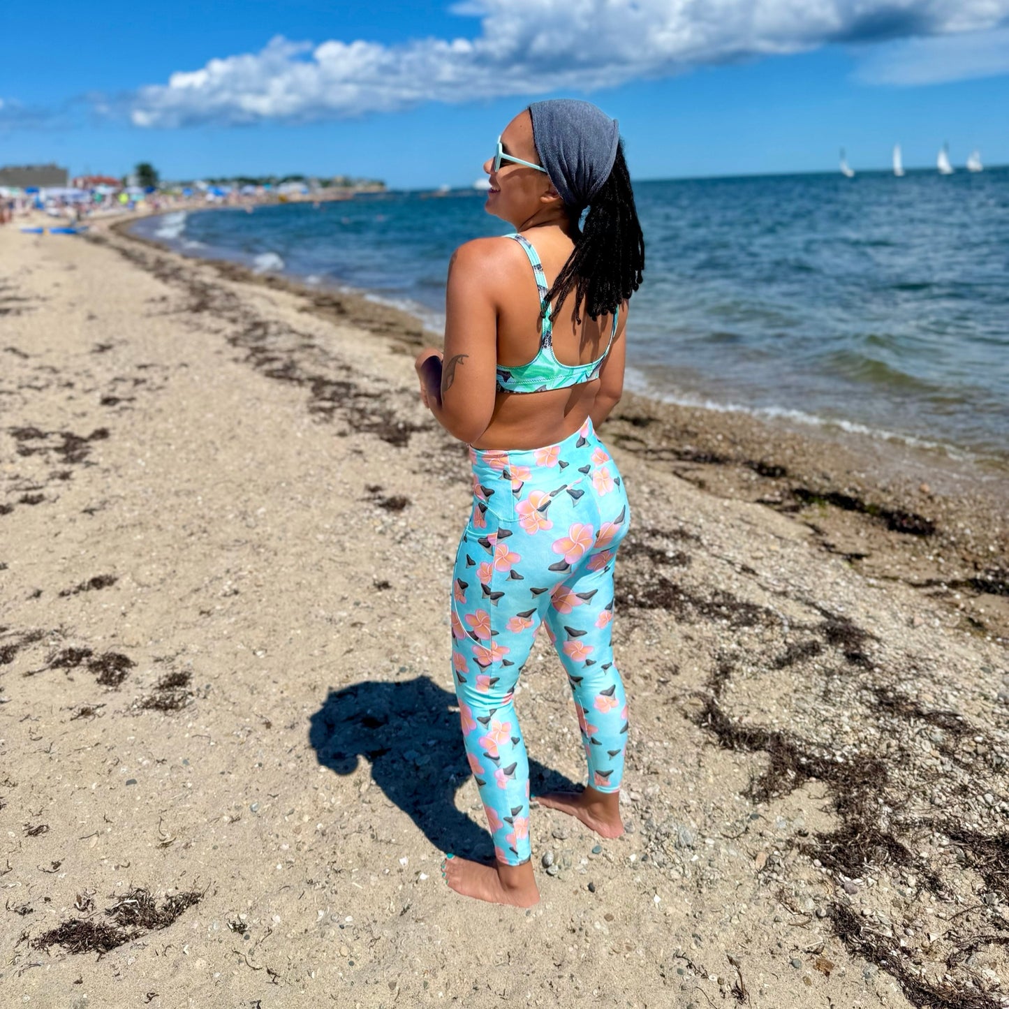 A teal and mint swirly background with Bull shark teeth and pinky orange plumeria flowers on our Shark Tooth Paradise Recycled Dive Leggings with pockets