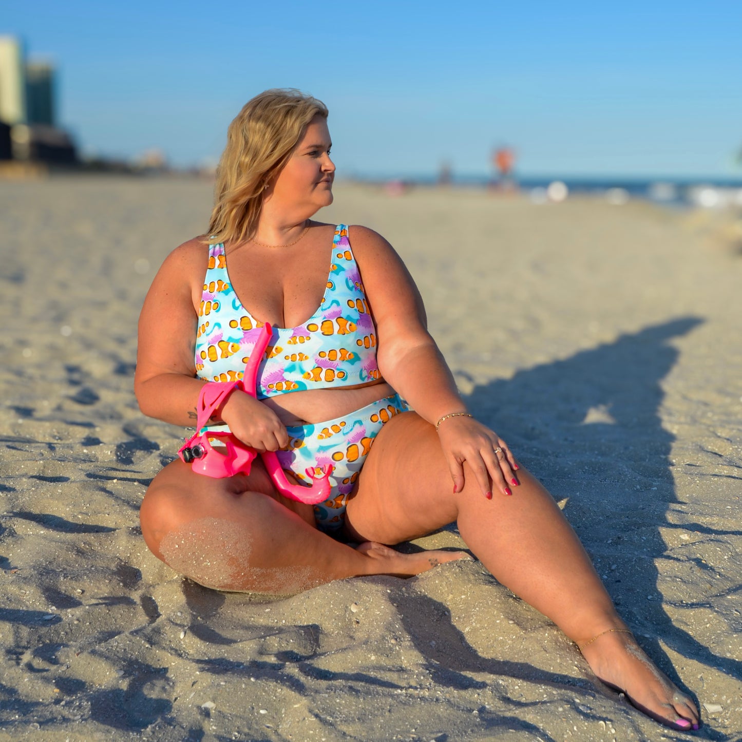 Woman sitting on the beach wearing a blue, pink and orange clownfish bikini