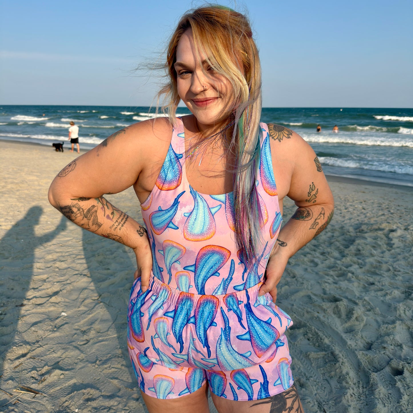 woman standing on a beach wearing a pink and colorful whale shark swimsuit and shorts 