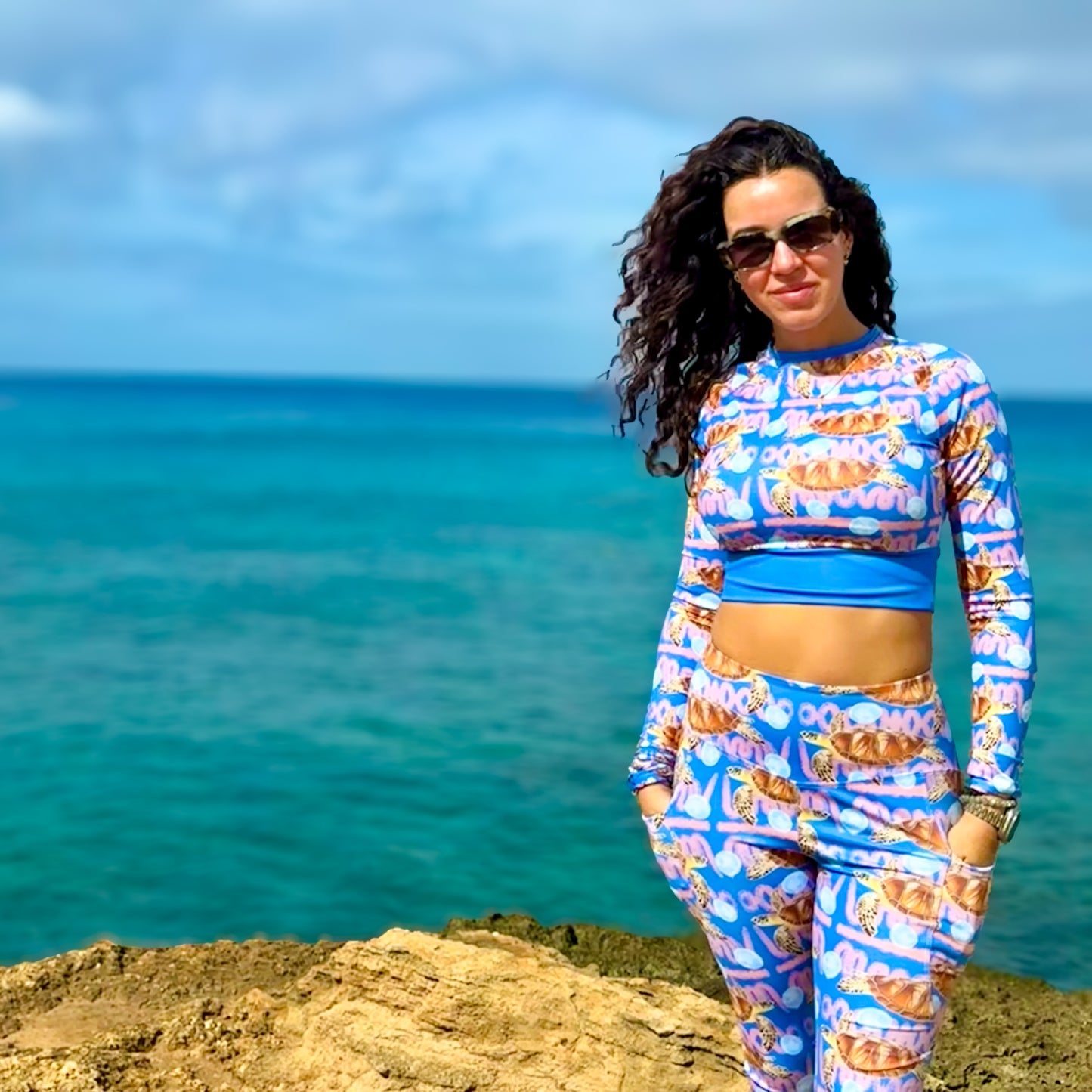 Angeline wearing the Royal blue and peachy background with sea turtles and moon jellyfish Eco dive leggings with the ocean behind her 