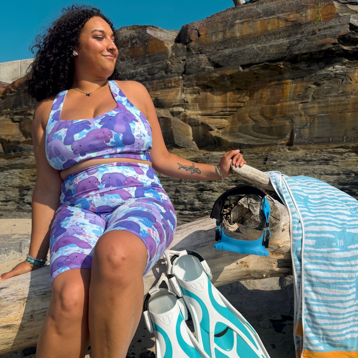 woman sitting on a log on a beach with dive gear wearing a purple and blue manatee activewear set 