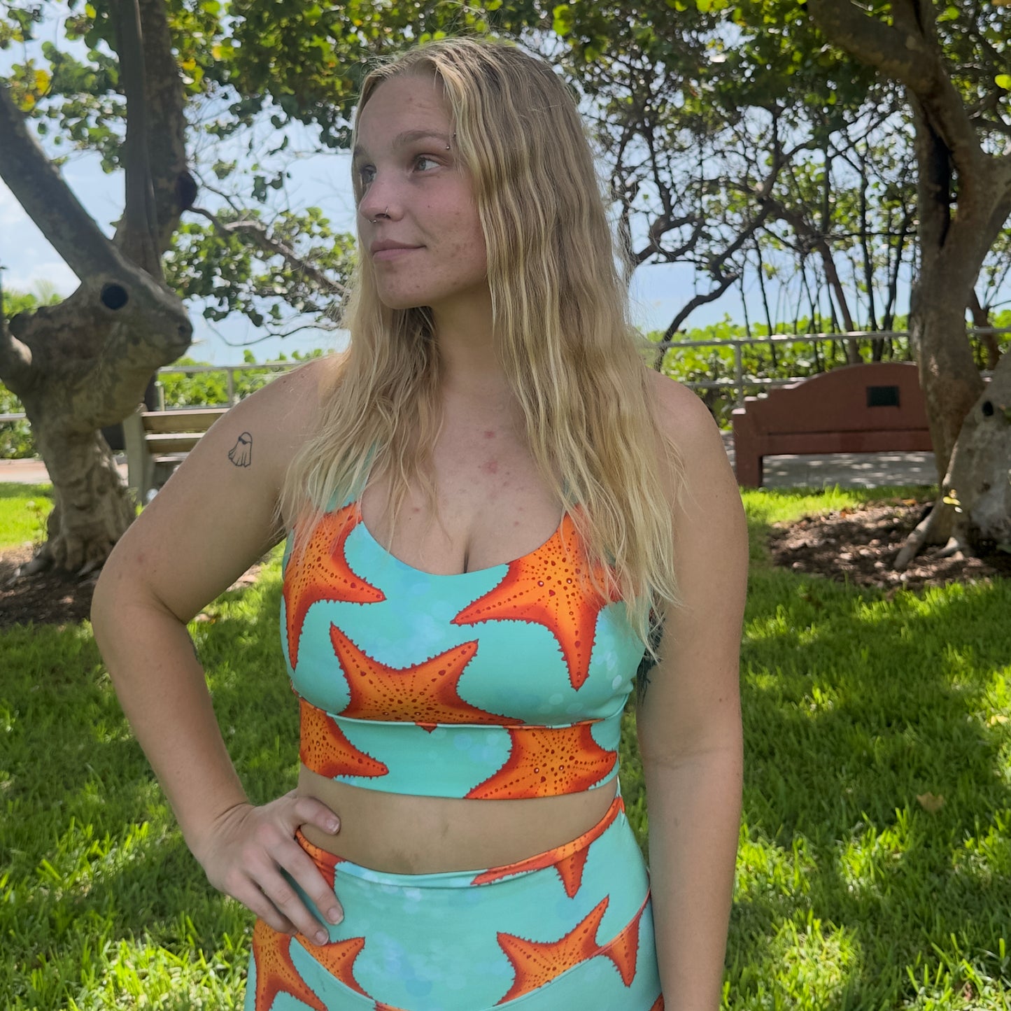 woman sitting in grass wearing a green/teal and orange starfish sports bra and matching shorts 