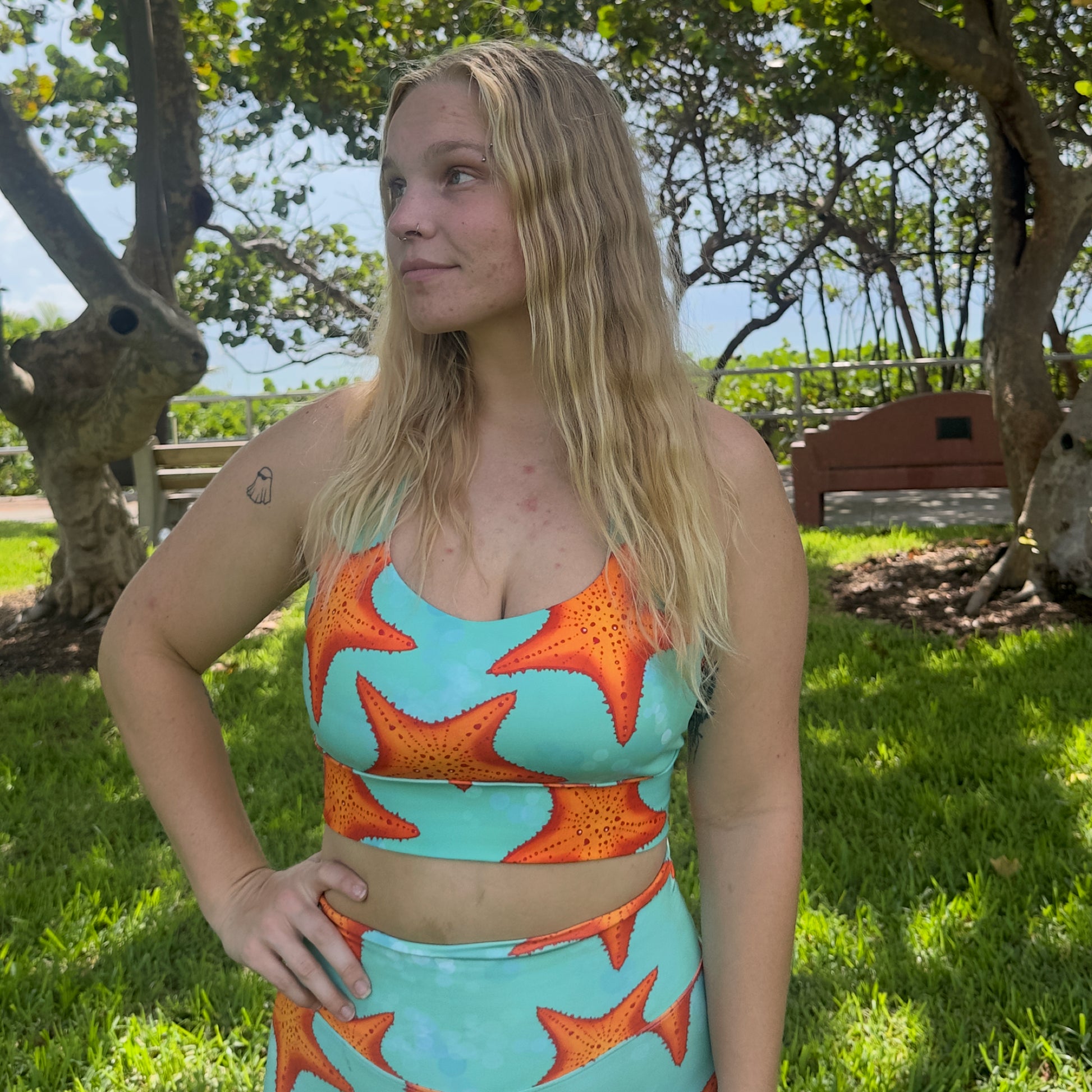 woman sitting in grass wearing a green/teal and orange starfish sports bra and matching shorts 