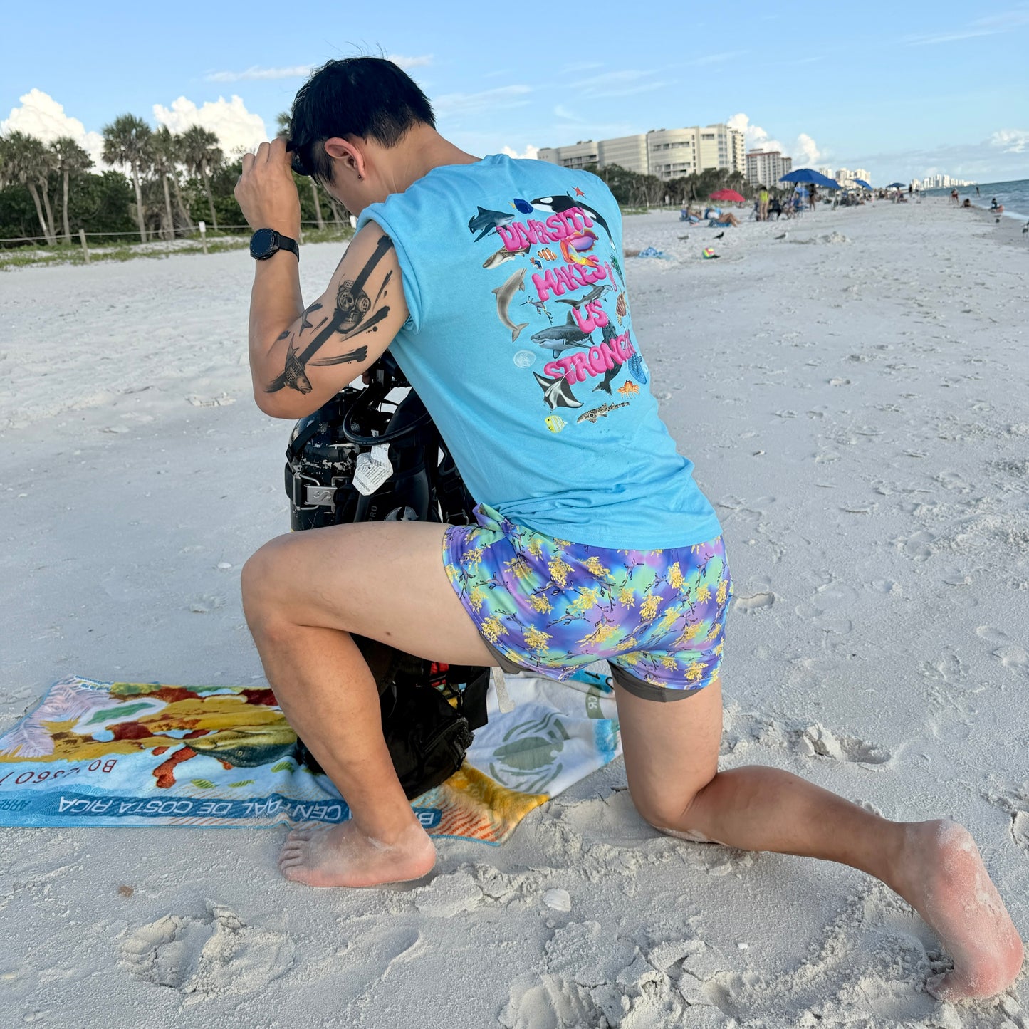 man kneeling on the beach with scuba gear wearing a blue t shirt with colorful ocean animals 