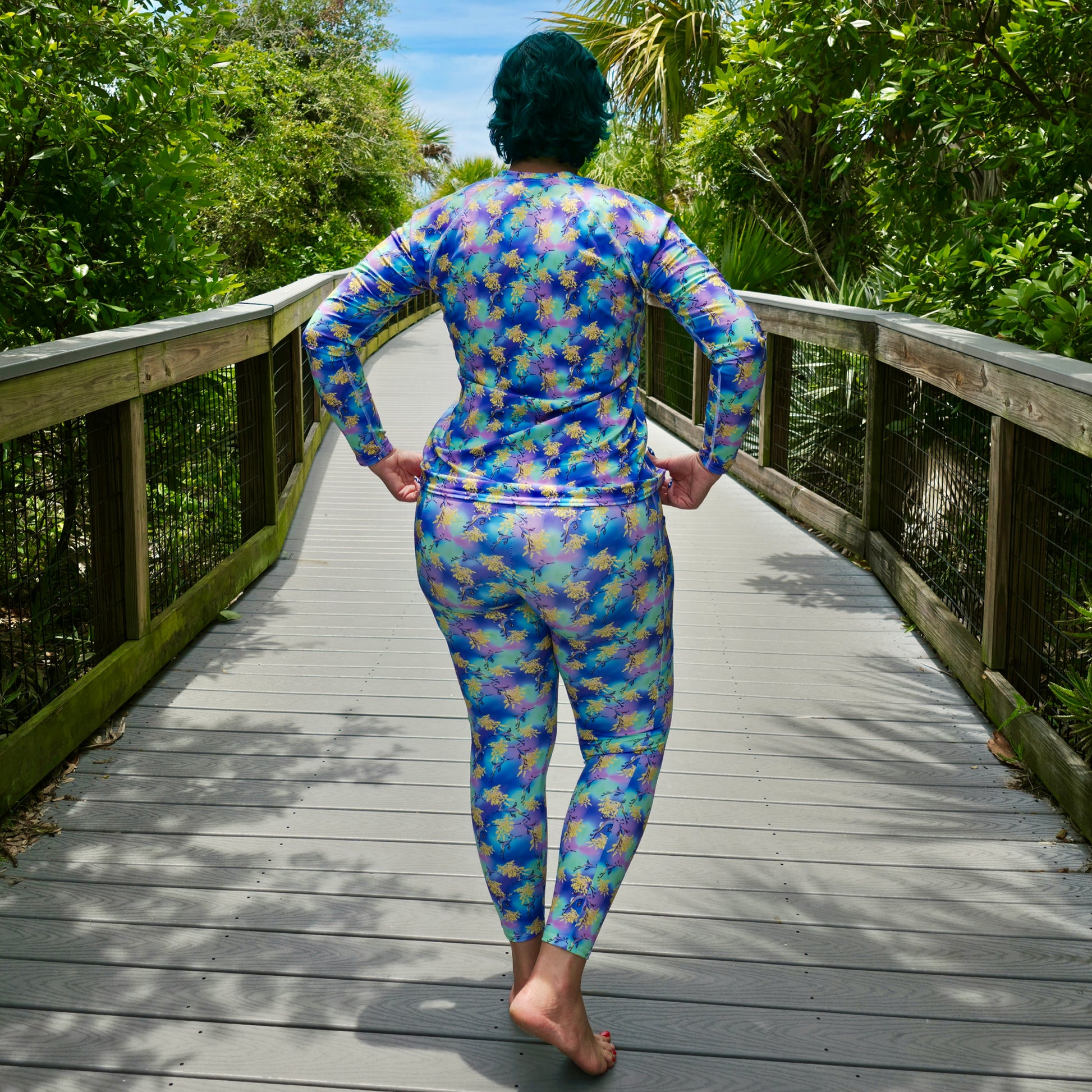 woman on a boardwalk wearing a pair of leggings that are purple, green, blue, yellow with sea dragons on it 