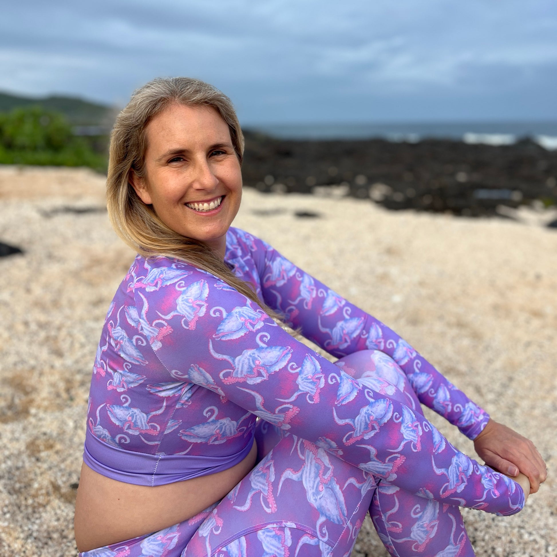 Krista wearing Purple and hot pink colorful octopus eco cropped rashguard on a rocky beach 
