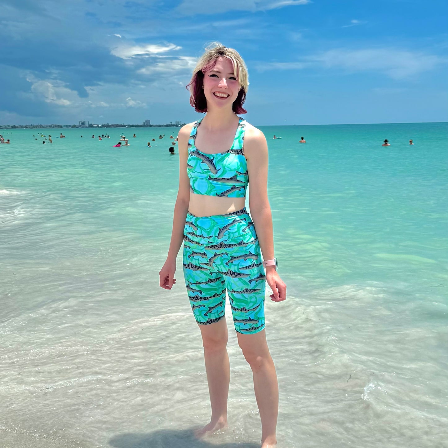 woman on the beach wearing blue leopard shark sports bra and bike shorts 
