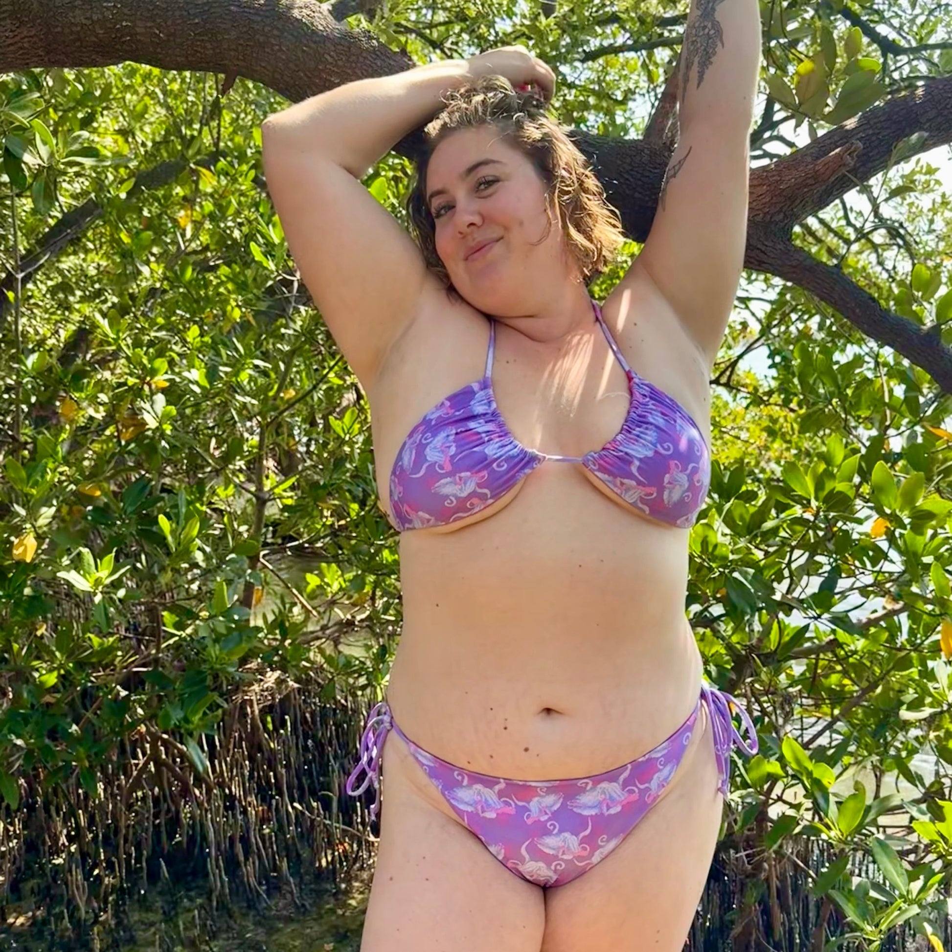 Layla wearing Purple and hot pink colorful octopus eco string bikini bottoms in front of some mangroves 