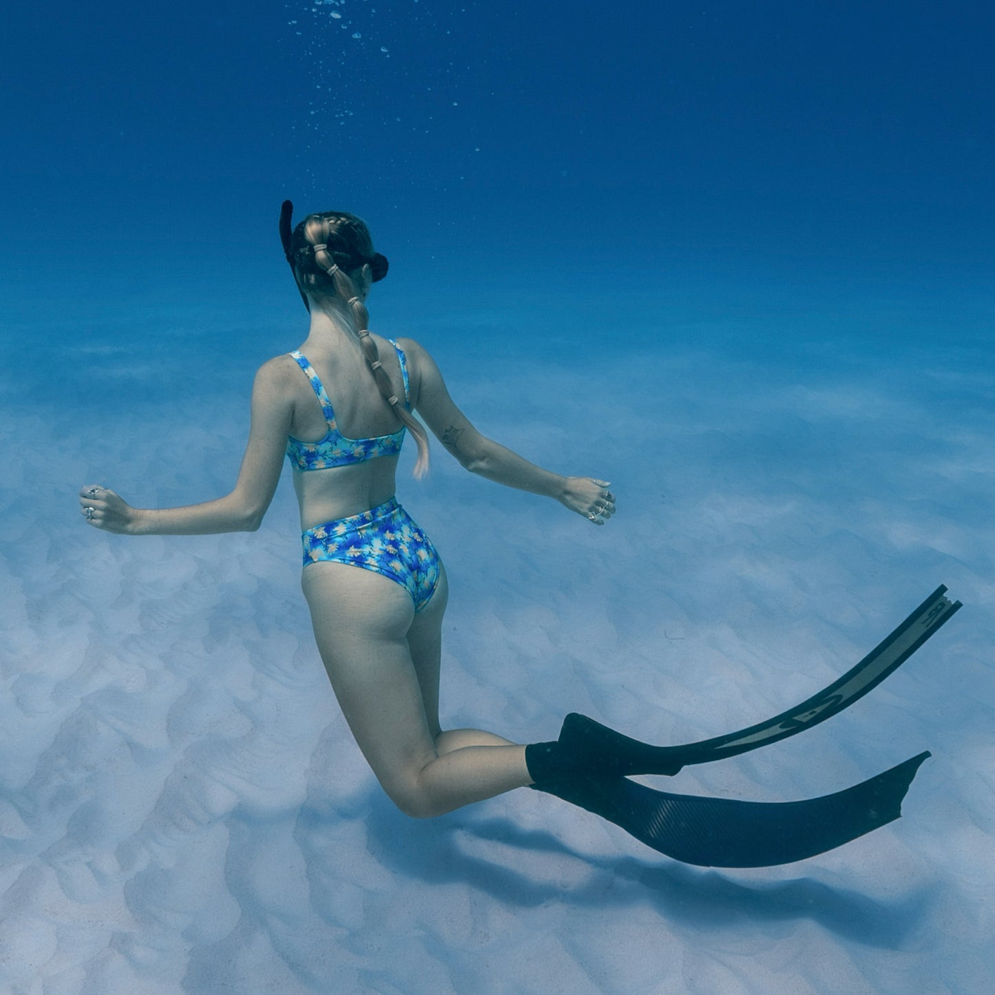 woman free diving underwater wearing a blue, purple, green, yellow sea dragon printed swimsuit 