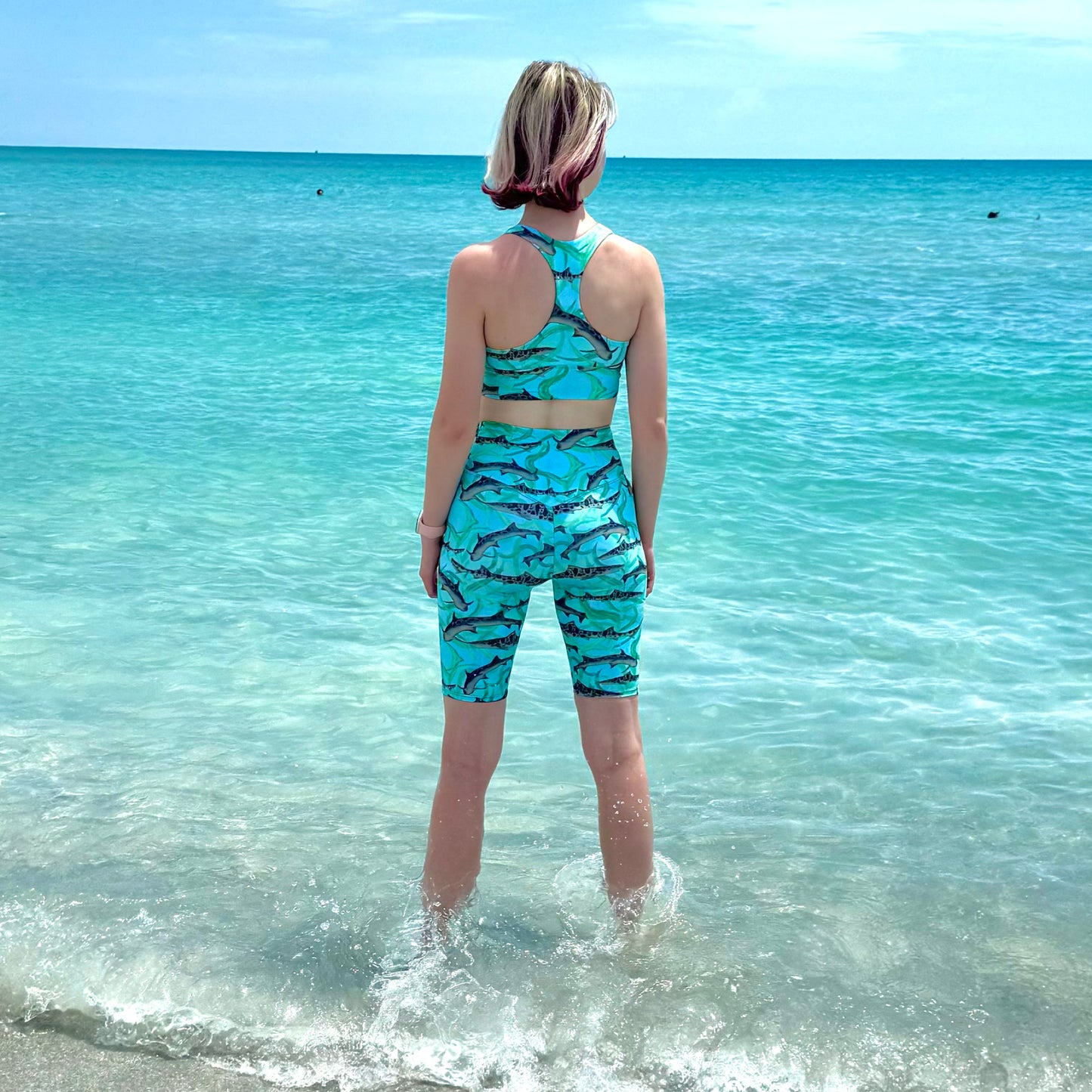 woman on the beach wearing blue leopard shark sports bra and bike shorts 