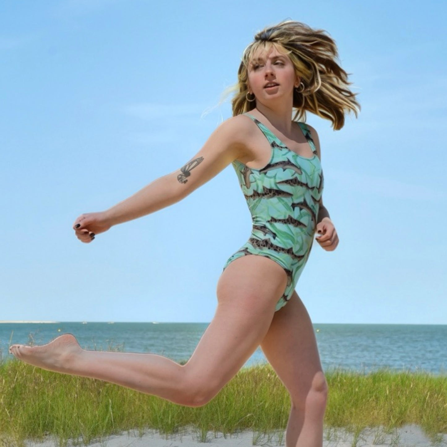 woman wearing a one piece swimsuit with teal and green and leopard sharks on it by the ocean