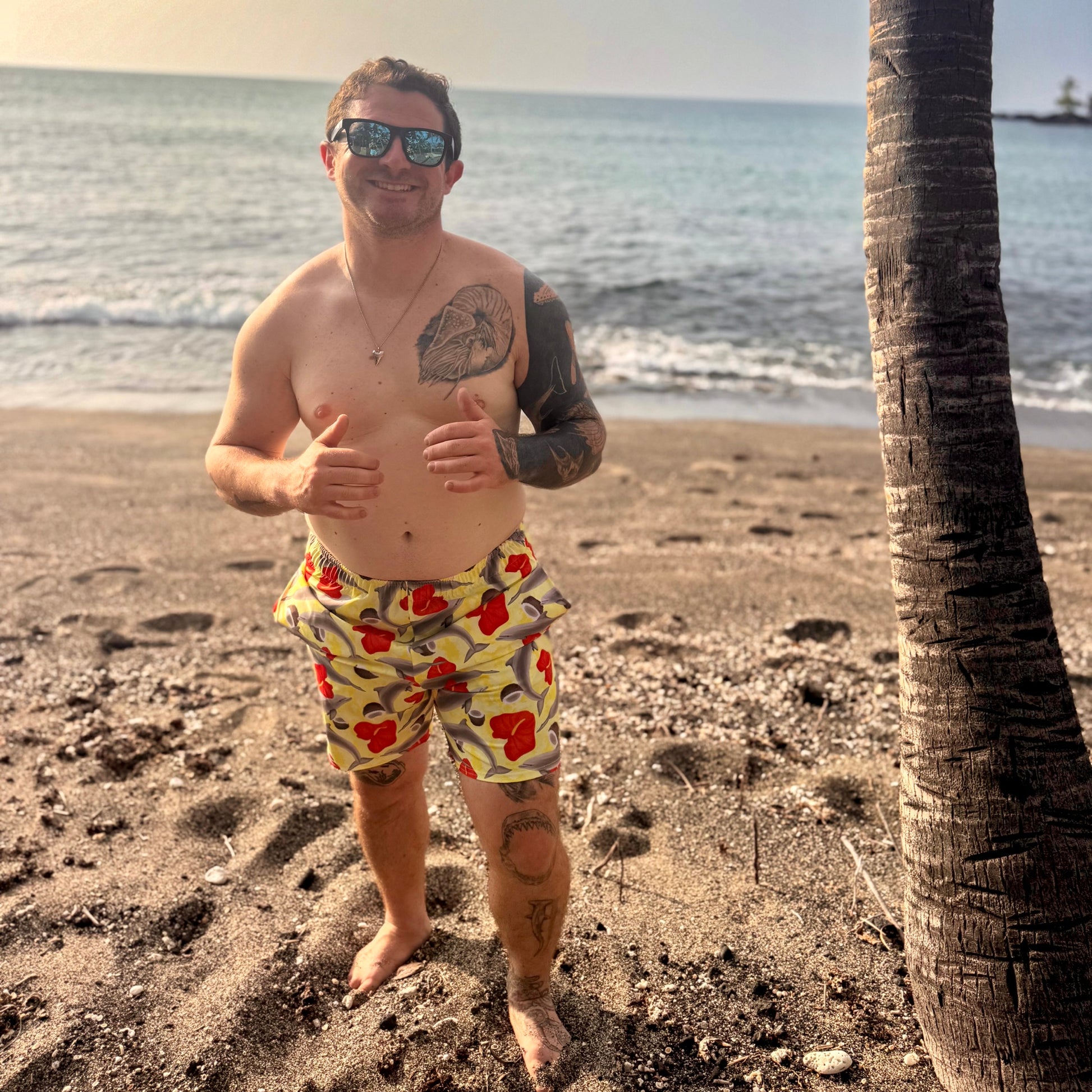 man on a beach by the water wearing yellow and red dolphin swim trunks 