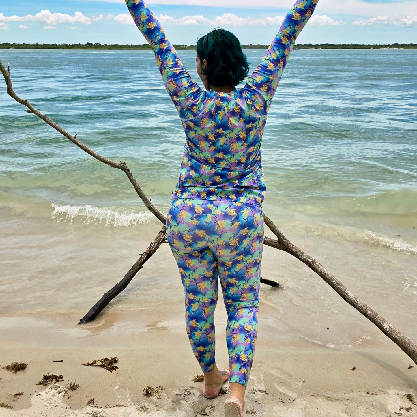 woman on the beach wearing a long sleeved rashguard that is purple, green, blue, yellow with sea dragons on it 