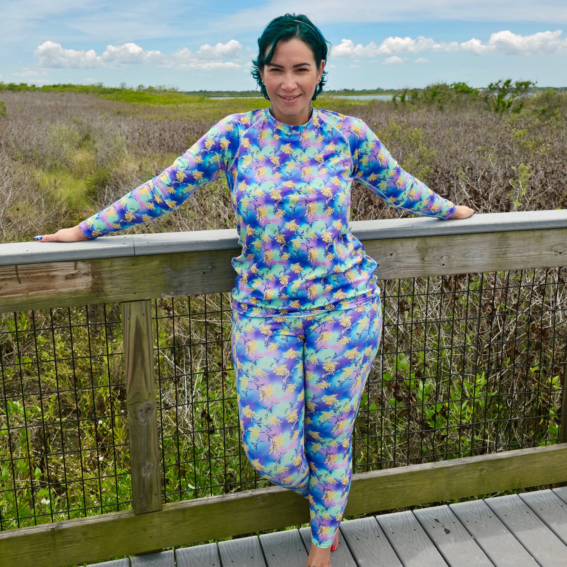 woman on a boardwalk wearing a pair of leggings that are purple, green, blue, yellow with sea dragons on it 