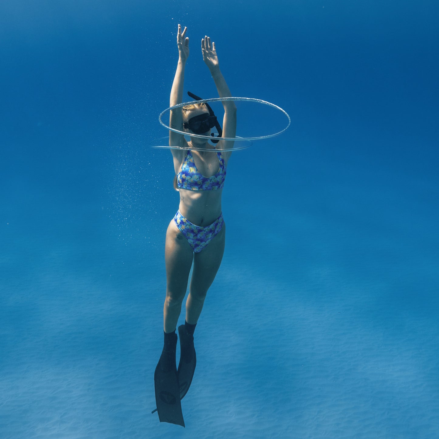 woman free diving underwater wearing a blue, purple, green, yellow sea dragon printed swimsuit 