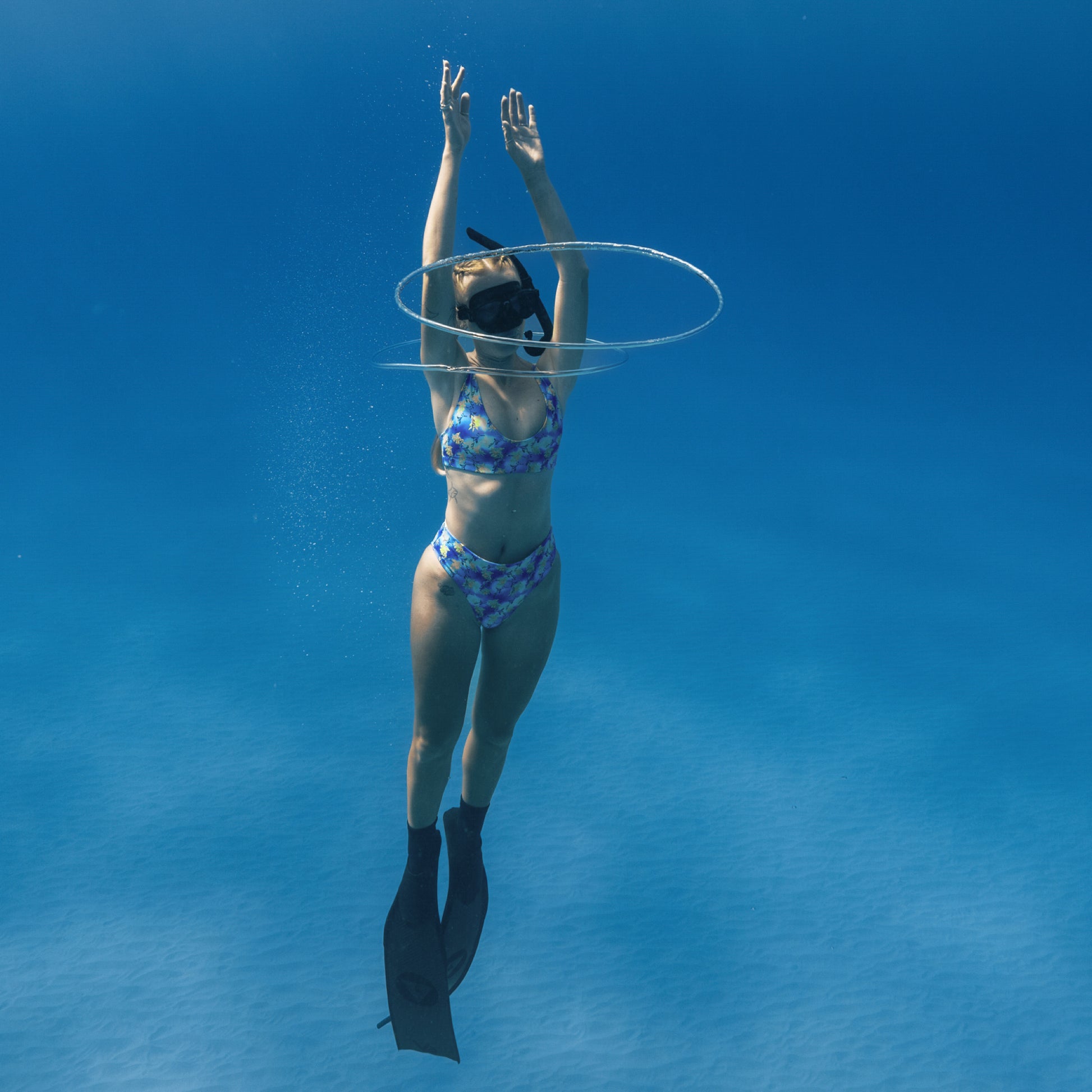 woman free diving underwater wearing a blue, purple, green, yellow sea dragon printed swimsuit 
