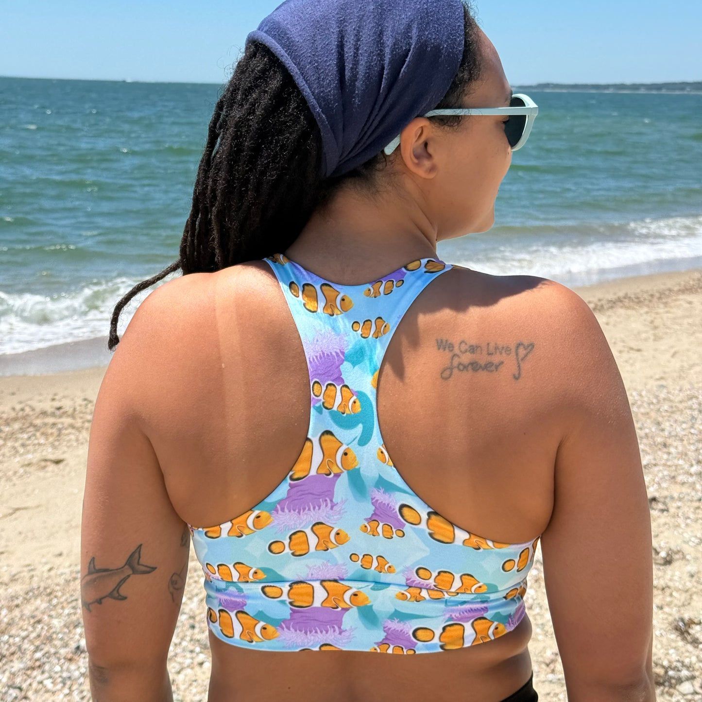 woman wearing a blue and pink sports bra with clownfish standing on the beach 