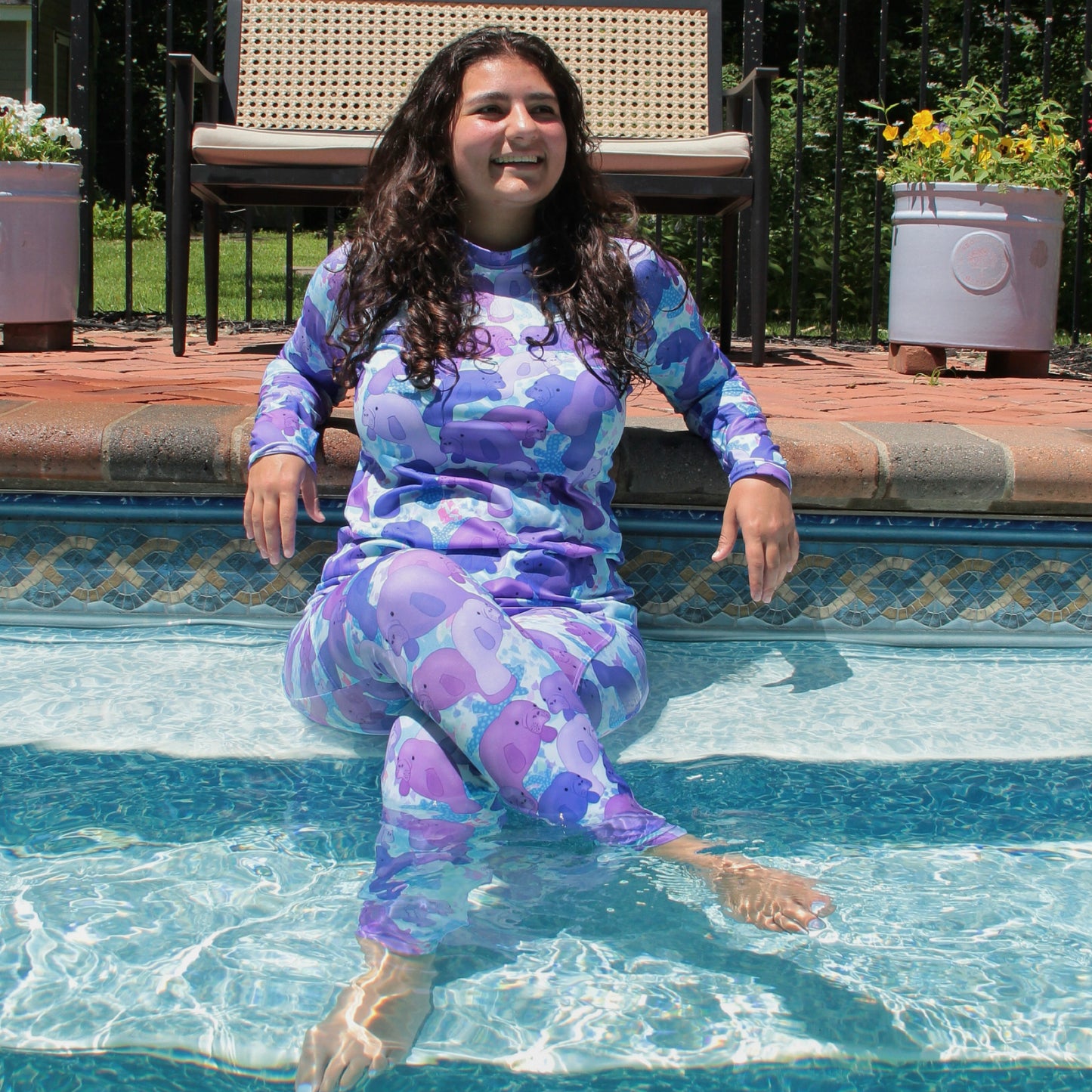 woman sitting in a swimming pool wearing a purple and blue rashguard with manatees 