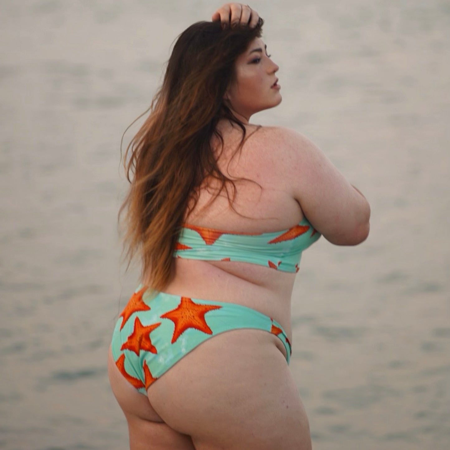 woman standing in water wearing a green/teal and orange starfish bikini facing away from the camera 