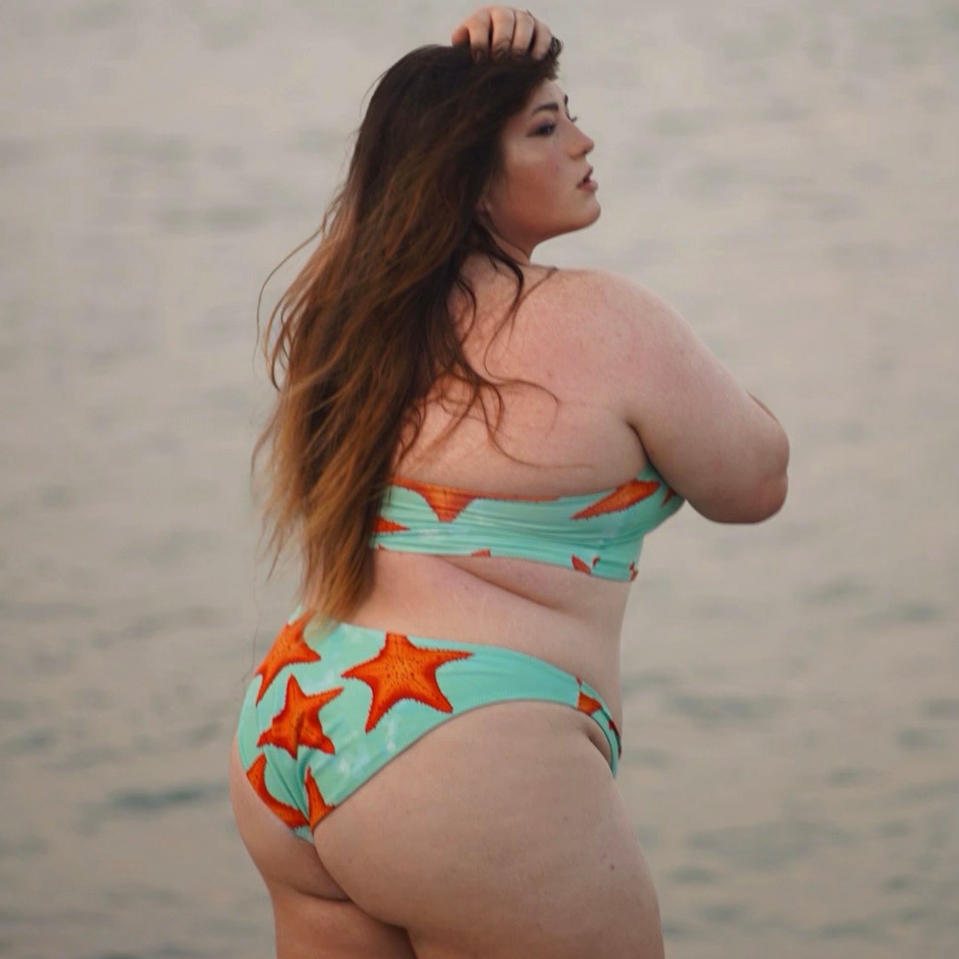 woman standing in water wearing a green/teal and orange starfish bikini facing away from the camera 