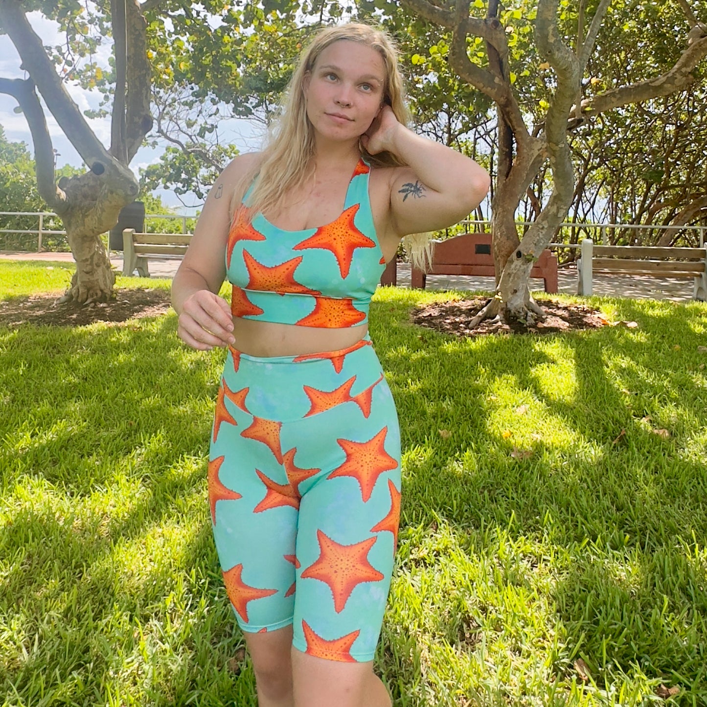 woman standing in a grassy park wearing green/teal and orange starfish bike shorts 