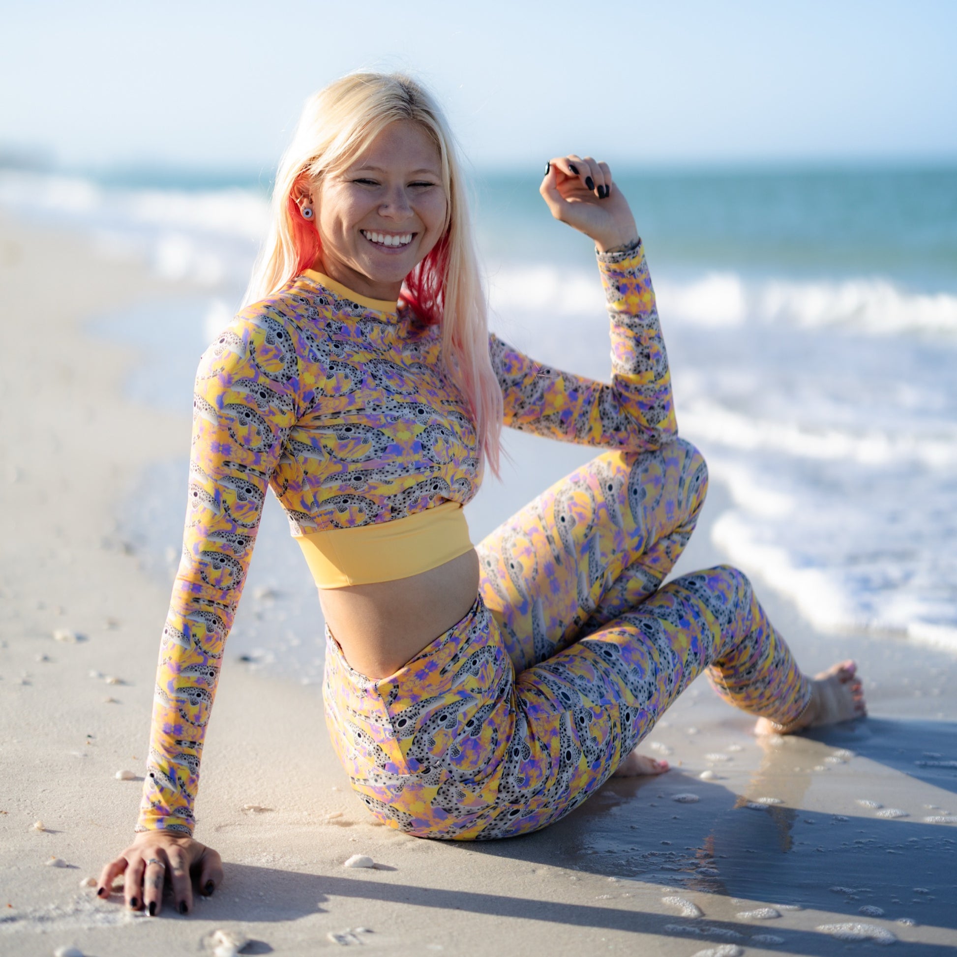 Nicole wearing an Epaulette Shark cropped rashguard with orange and purple background on the beach 