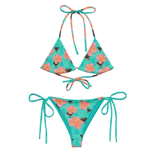 A teal and mint swirly background with Bull shark teeth and pinky orange plumeria flowers on our Shark Tooth Paradise Recycled String Bikini 