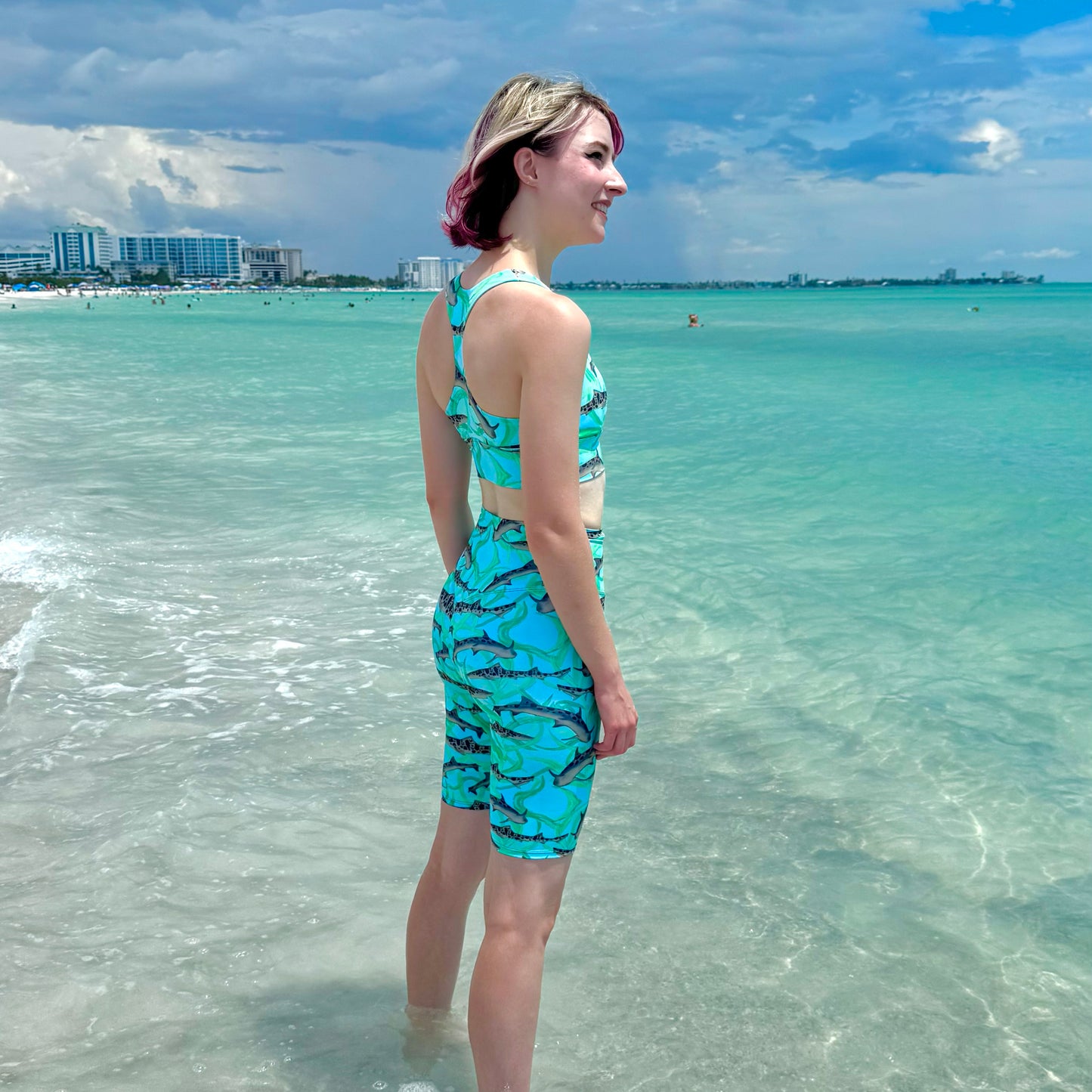 woman on the beach wearing blue leopard shark sports bra and bike shorts 