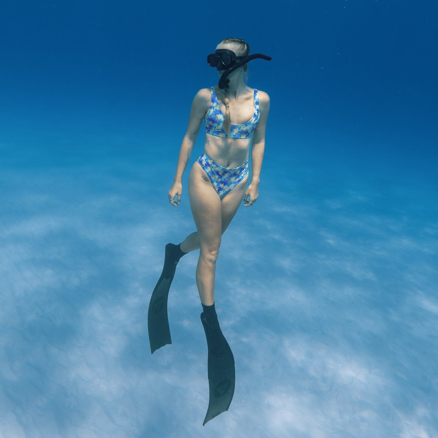 woman free diving underwater wearing a blue, purple, green, yellow sea dragon printed swimsuit 