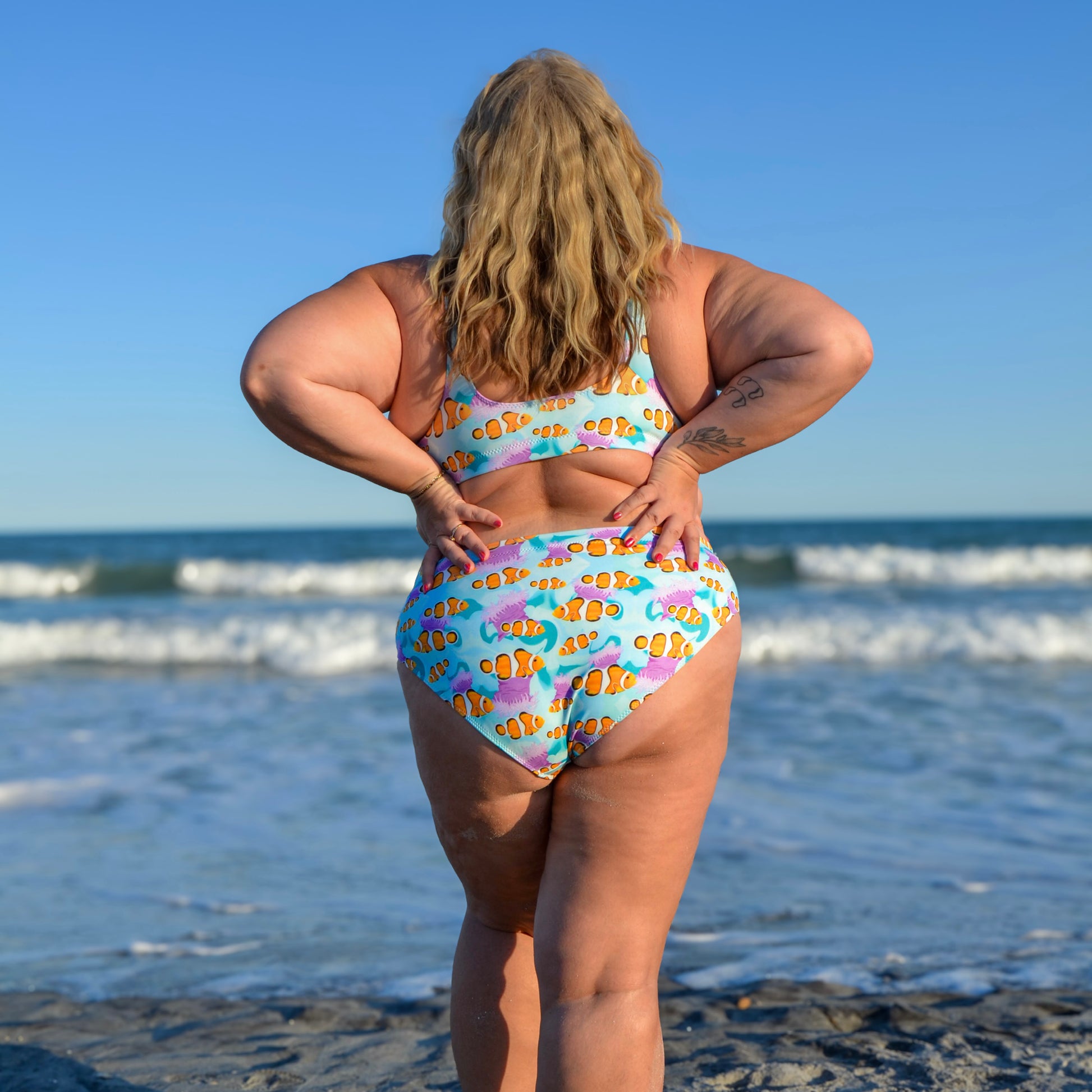 Woman standing in front of the ocean wearing a blue, pink and orange clownfish bikini 