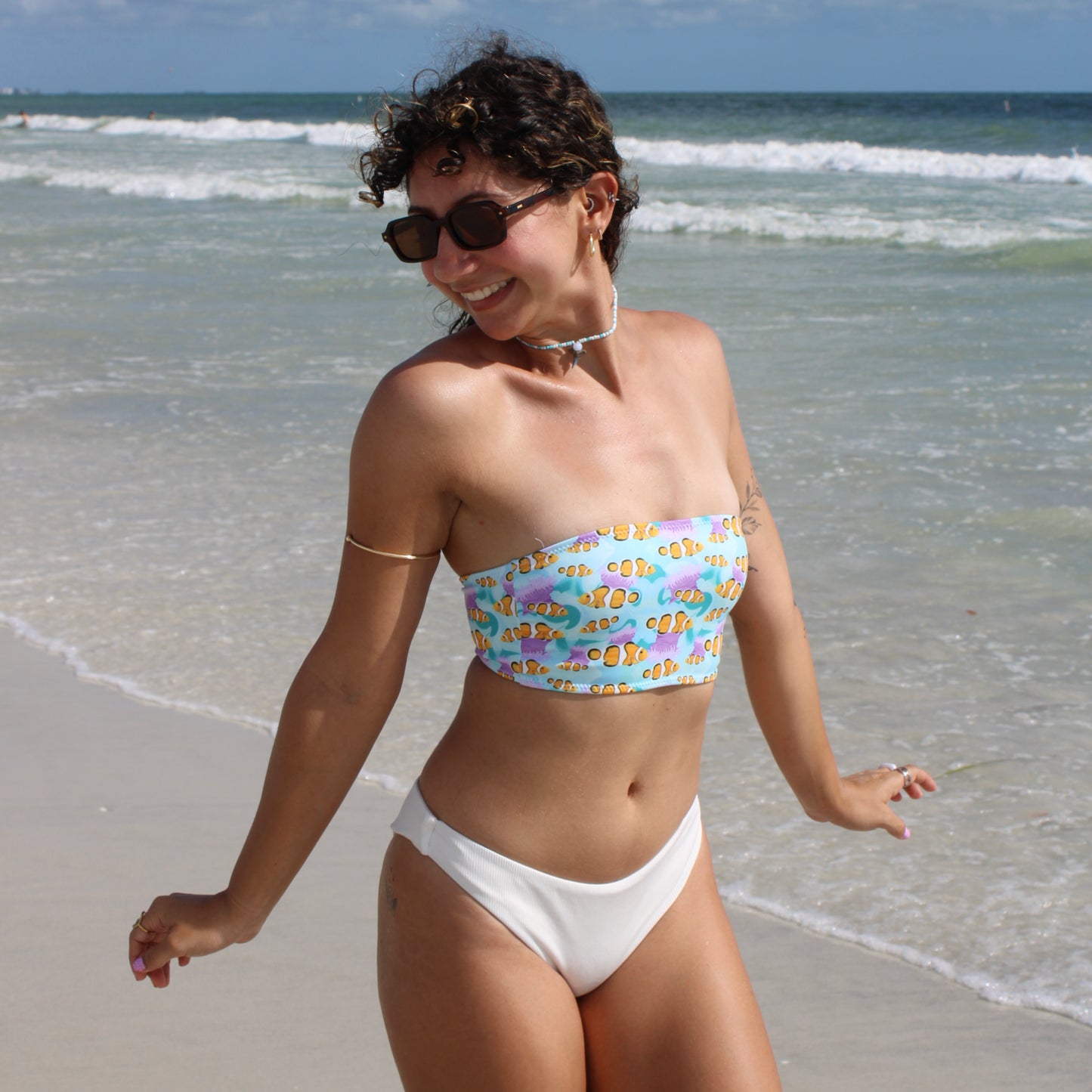 woman wearing a blue and pink strapless bikini top with clownfish standing on the beach 