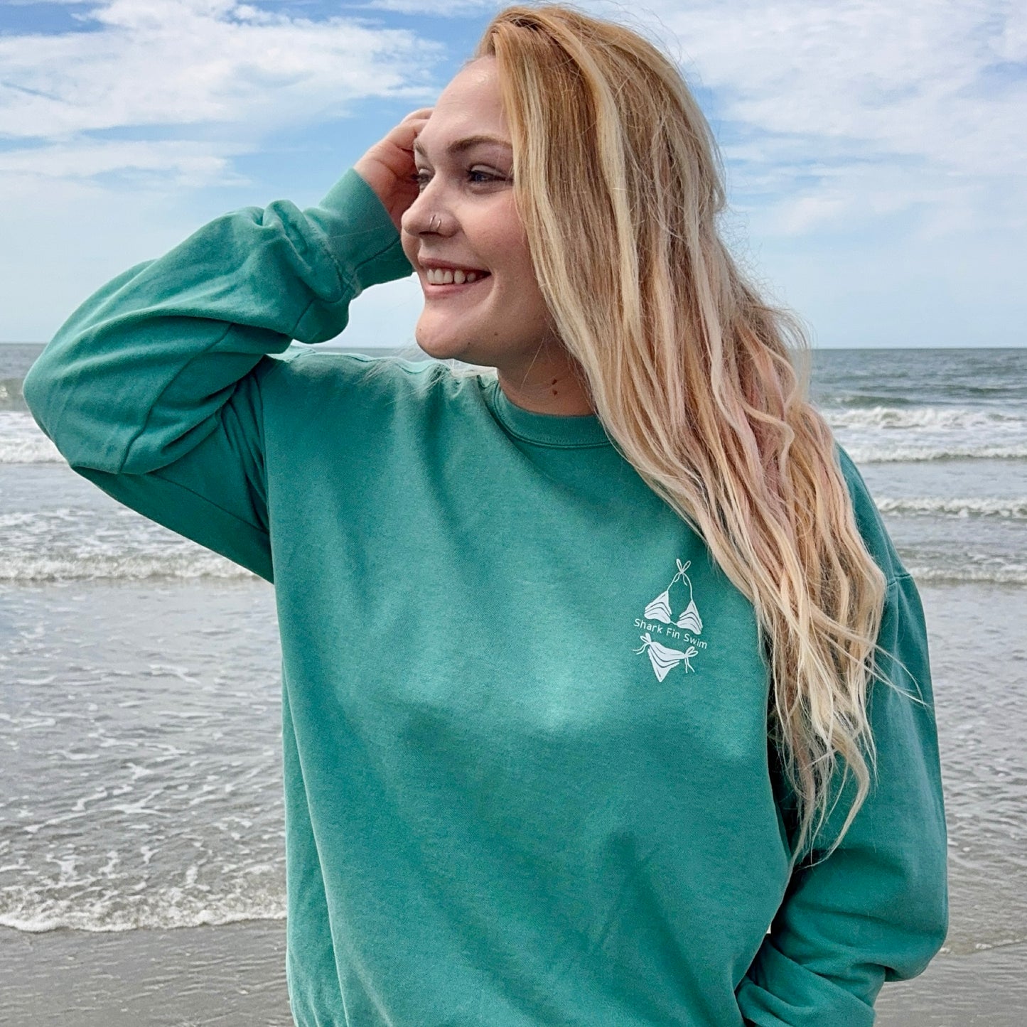 Woman wearing a green sweatshirt with a logo on a beach