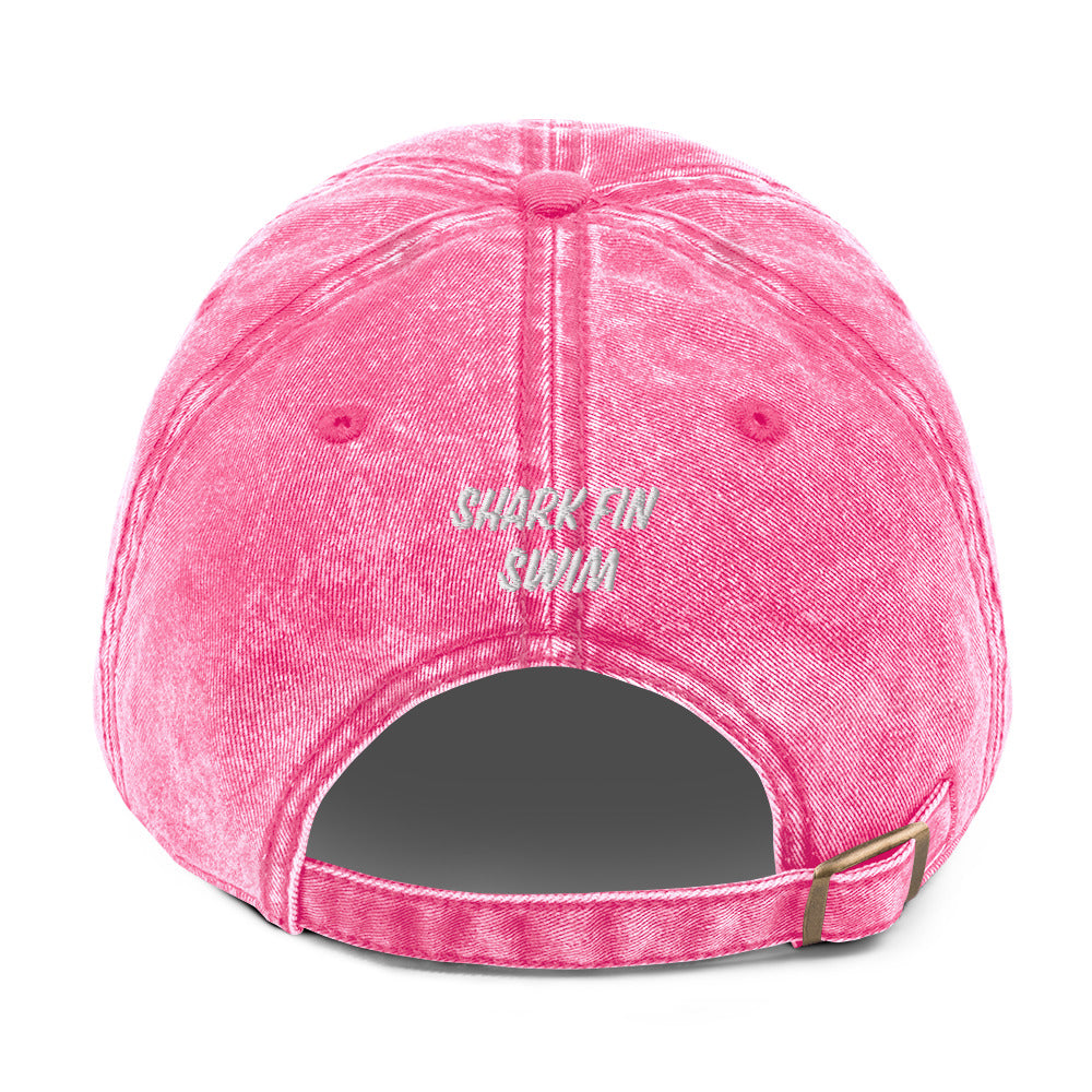 Pink baseball cap with embroidered text “shark fin swim” and adjustable back strap with metal buckle 