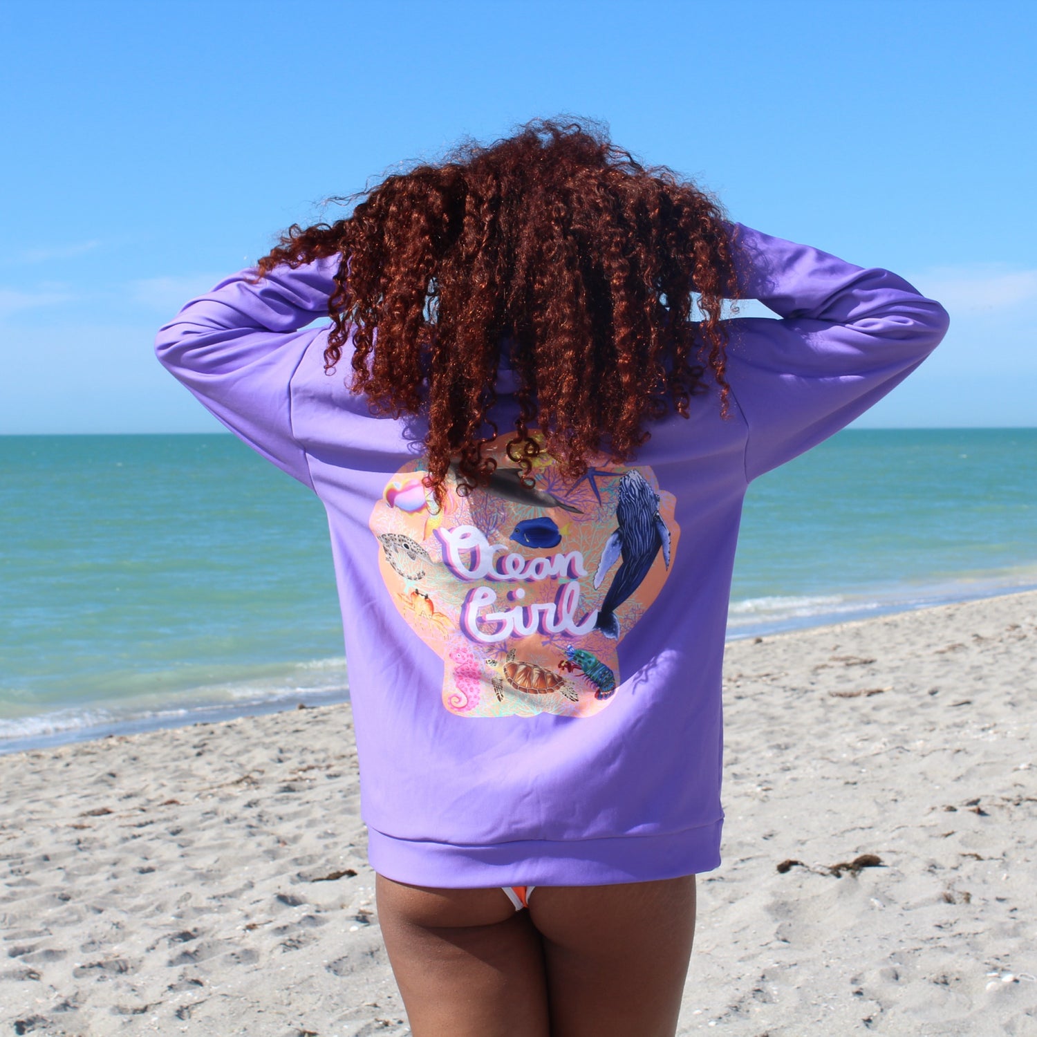 Person wearing a purple hoodie with 'Ocean Girl' design on a beach