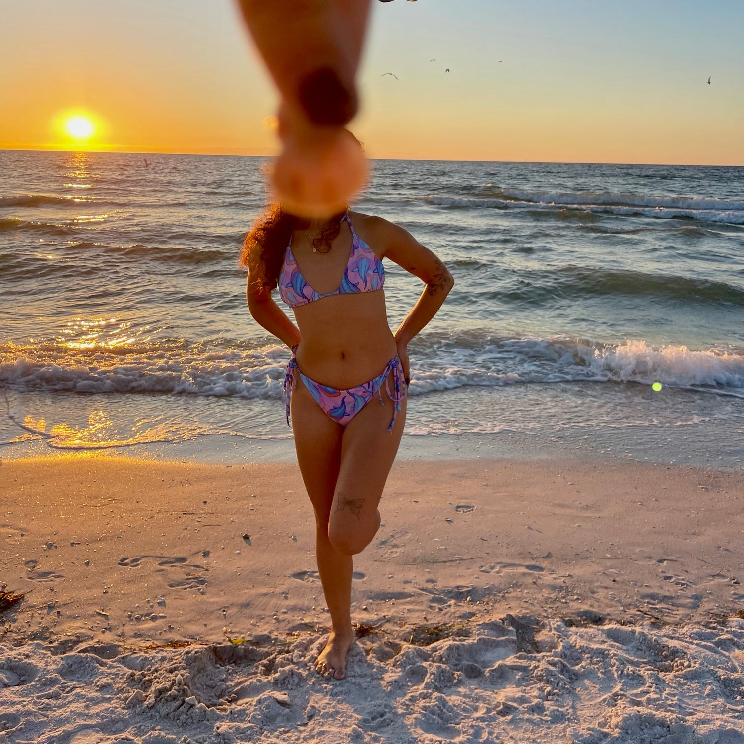 Nicole wearing the rainbow bubblegum string bikini on the beach with a seashell over her face 
