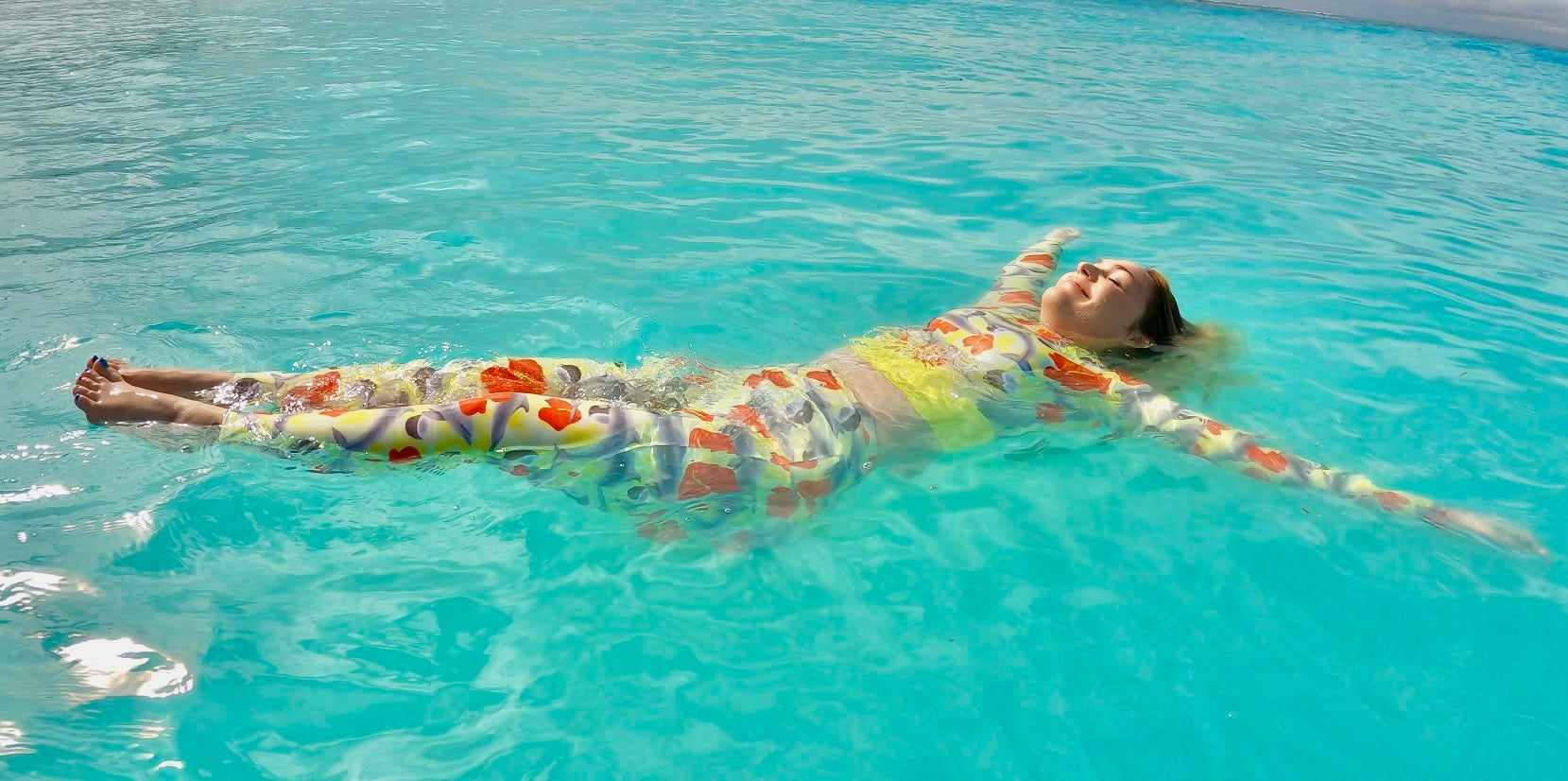 Woman floating in blue water wearing a yellow and red dolphin cropped Rashguard and leggings 