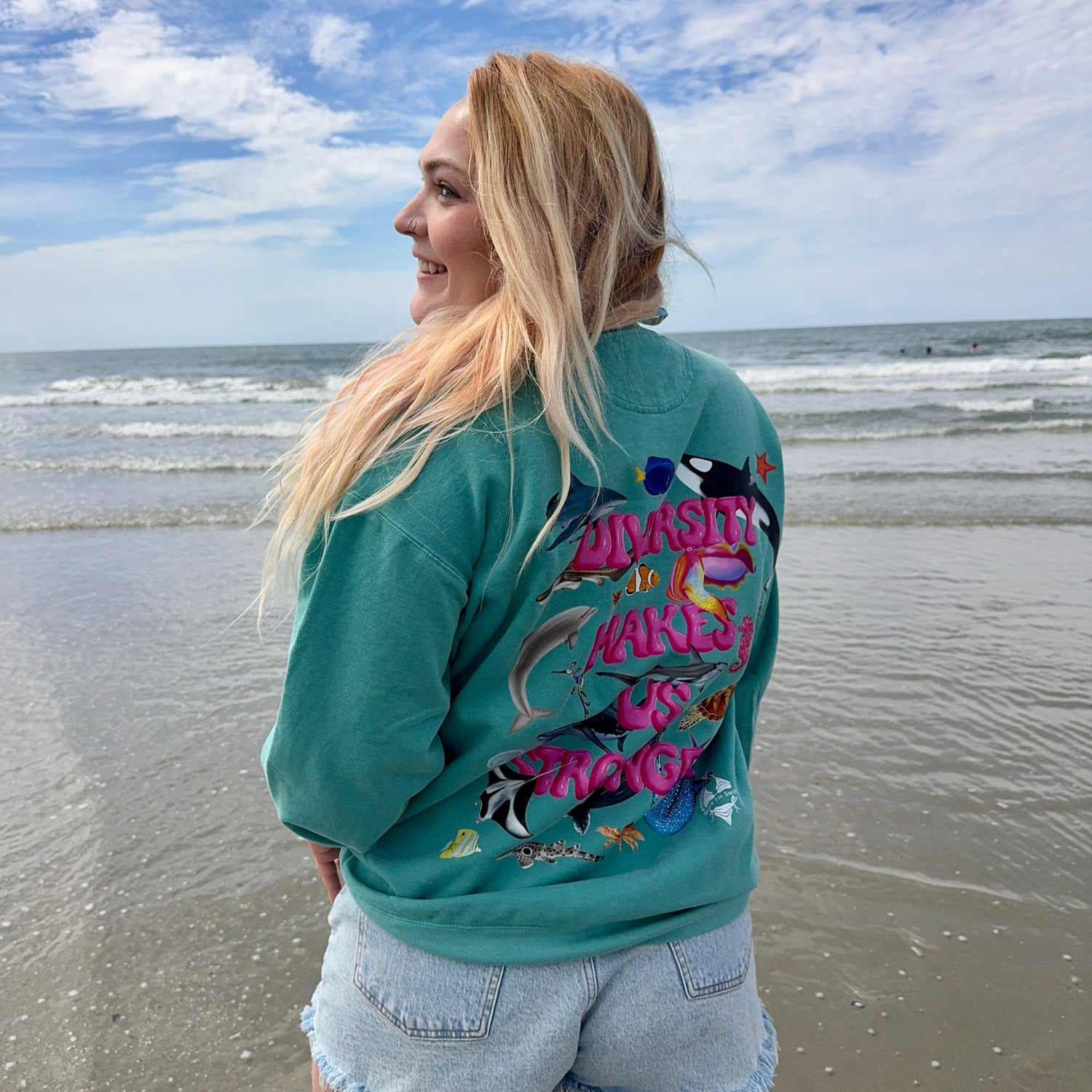 Woman on a beach wearing  green ocean animal sweatshirt 