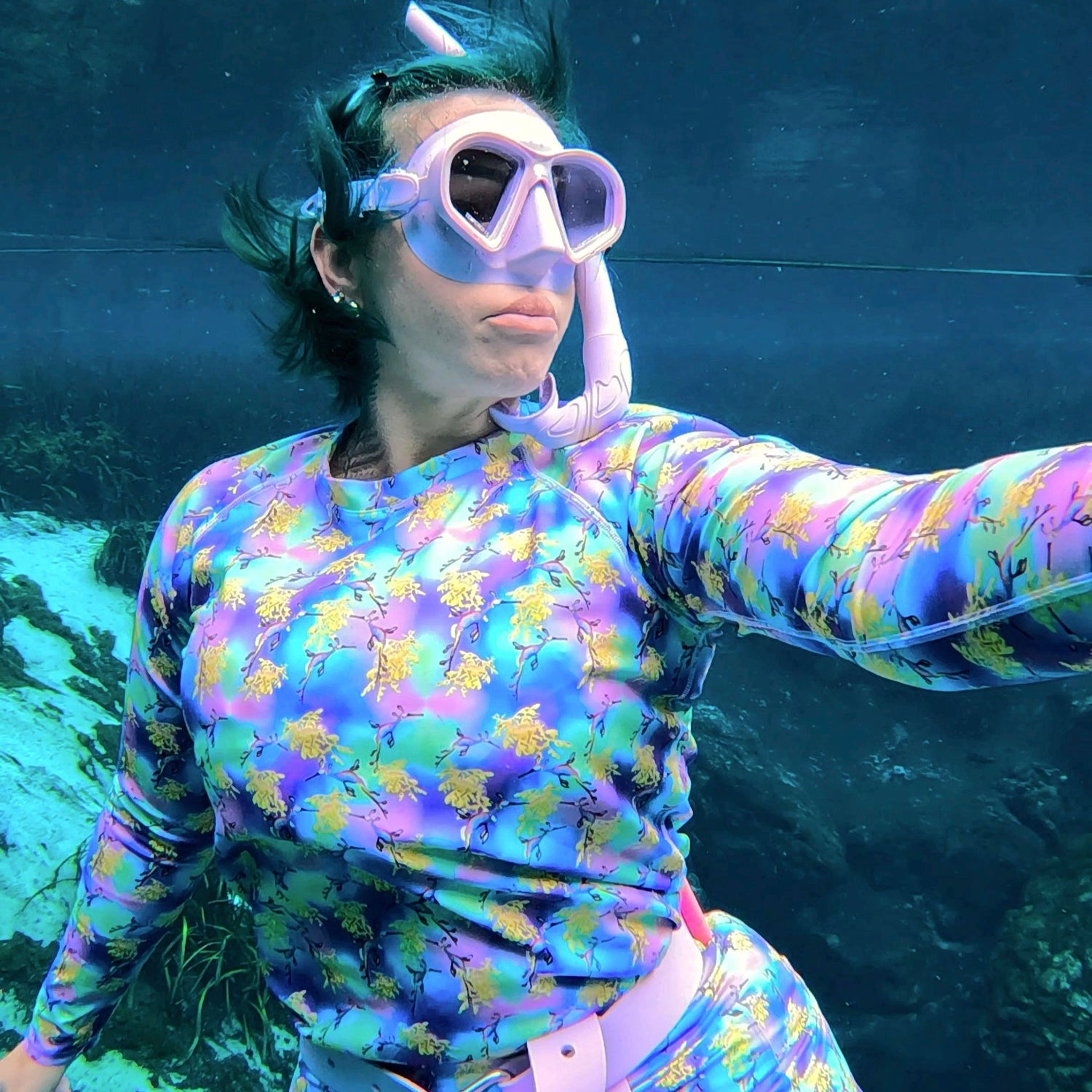 Woman diving underwater wearing a green, purple and Yellow Sea dragon rashguard 